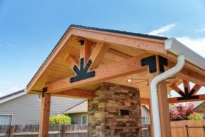A wooden pavilion structure featuring a stone fireplace and decorative black metal bracing.