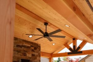A black ceiling fan with integrated lights mounted to a wooden tongue-and-groove ceiling under a covered patio.