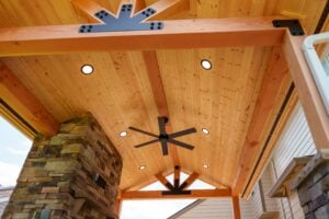 Covered patio with a wood-plank ceiling, recessed lighting, a ceiling fan, and a stone fireplace.