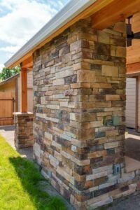 A large stone-faced pillar supporting a wooden patio roof overhang.