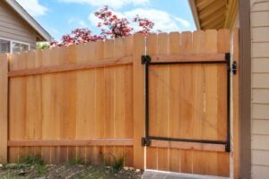 A light wood picket fence with a matching gate featuring a black metal frame and diagonal support wire.