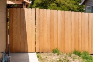 A wooden privacy fence with a gate, installed beside a house.