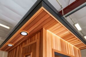 Exterior corner of a wood-paneled structure featuring recessed round lights and strip lighting under the roof overhang.