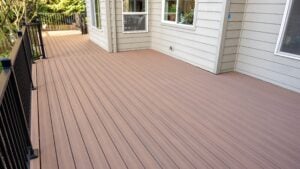 A spacious, clean wooden deck attached to a light-colored house with black railings and multiple windows, overlooking a leafy backyard.