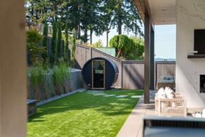 A circular barrel sauna sits on a manicured lawn in a backyard patio area.