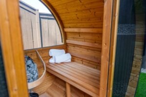 The interior of a wooden barrel sauna featuring a bench with folded white towels and a stone-filled heater.