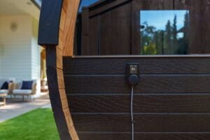 A digital temperature controller set to 82 degrees mounted on the exterior of a dark wood barrel sauna.