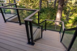 Wooden deck with glass-paneled railings and stairs leading down toward a forest.