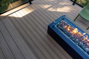 Rectangular black fire pit with a glass wind guard and glowing embers on a composite deck.