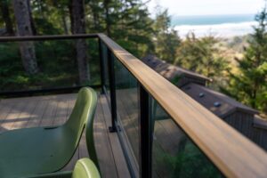 Two green chairs on a wooden deck overlooking a forest, a house roof, and the ocean.