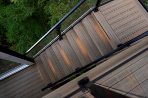 A wooden outdoor staircase with illuminated steps and a glass railing, viewed from above.