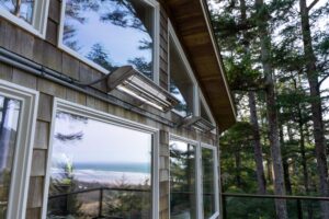 Two mounted outdoor heaters attached to the shingled exterior wall of a cabin overlooking the ocean and forest.