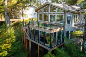 Multi-story home with a wrap-around glass deck overlooking a forested landscape.