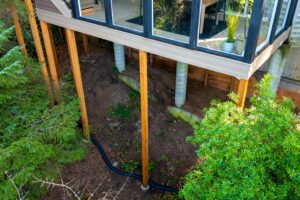 High-angle view of a house deck supported by wooden posts and concrete pillars over a sloped dirt yard.