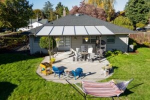 Aerial view of a backyard patio with a covered seating area, a hammock, and blue adirondack chairs on a grassy lawn.