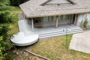 An elevated view of a gray house with a wide, multi-level deck, including a porch swing and a rounded seating area.