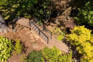 An aerial view of a wooden staircase with black metal railings descending through a wooded garden.