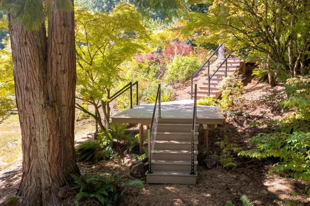 Wooden staircase with metal railings leading to a landing in a wooded garden.