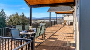 A covered wooden deck featuring a dining table with chairs and a view of a river and distant hills.