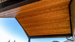 An angled view of an outdoor ceiling made of horizontal wood planks with a clear blue sky in the background.