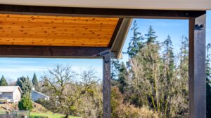 A wooden patio cover with a cedar tongue-and-groove ceiling overlooking a forest of evergreen trees.