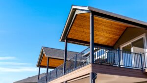 A house with two covered, elevated wooden decks featuring black railings against a clear blue sky.