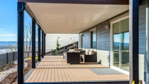 Covered wooden deck with wicker patio furniture, overlooking a fenced backyard and distant hills.
