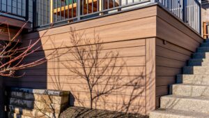 Brown composite deck skirting with a dark tree shadow cast across the boards, adjacent to stone steps.