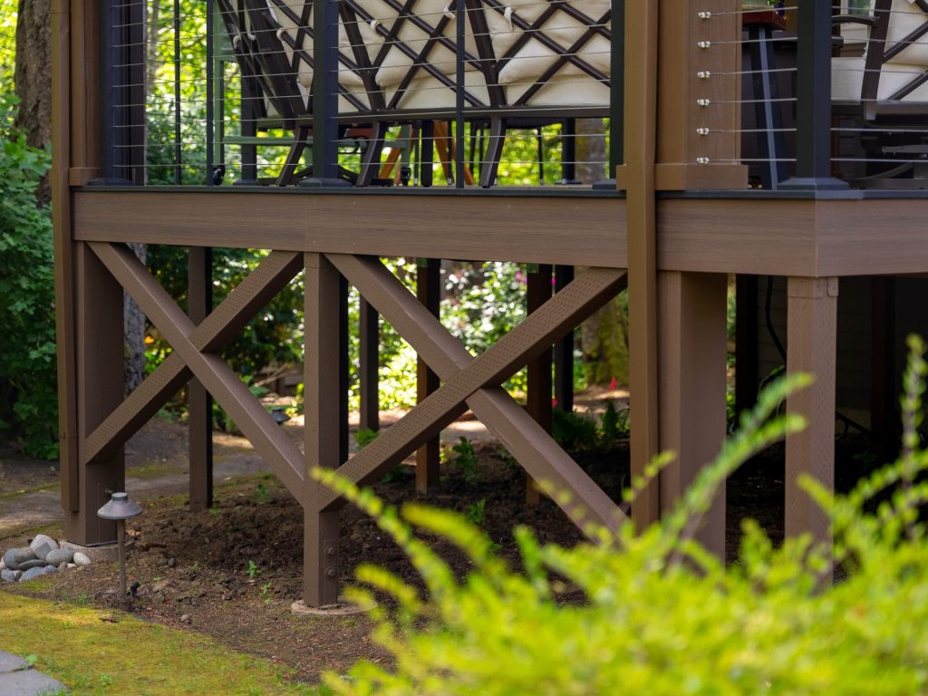 A close-up view of the wooden support structure beneath a raised outdoor deck, surrounded by greenery and small garden lights.