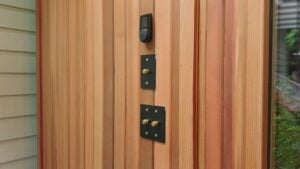 A modern smart thermostat and two black rectangular light switch plates with brass knobs mounted on vertical wood paneling.